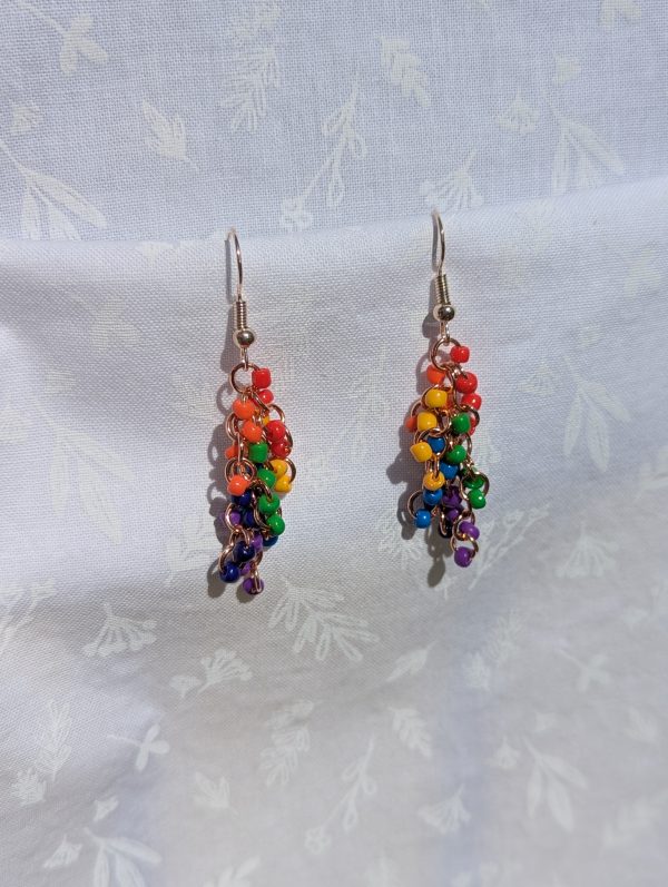 A pair of long, dangling rainbow beaded earrings featuring 24 colorful glass seed beads per earring, attached to rose-gold-colored jump rings and rose-gold-colored hooks.