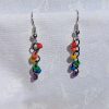 A pair of handmade mini rainbow earrings featuring six colorful glass seed beads—red, orange, yellow, green, blue, and purple—linked with pewter-colored jump rings and silver-colored earring hooks, displayed against a white fabric background.