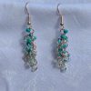 The Seafoam green and teal earrings feature a blend of teal glass seed beads of various hues each with a variety of texture. A total of 18 beads per earring—three beads per hue—cascade gracefully, creating a vibrant and eye-catching effect.