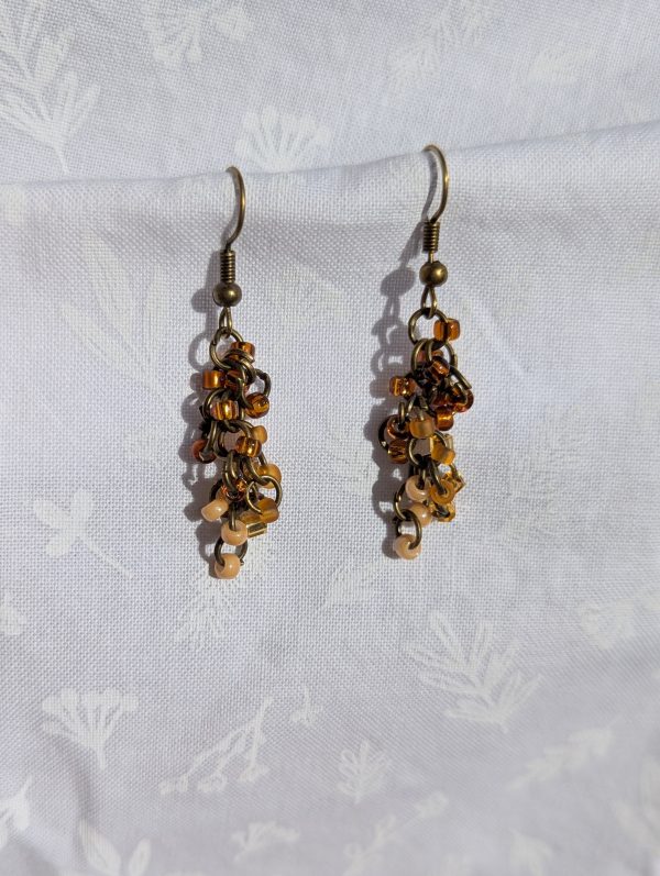 The Mocha Dusk Earrings radiate warmth and charm with their cascading design. Each earring features a total of 18 glass seed beads in vibrant brown, tan, and cream shades, carefully arranged with antique bronze-colored jump rings for a rustic yet elegant finish.