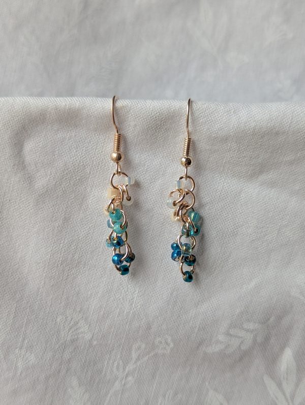 Ocean Tide earrings with 14 beads in seven ocean-inspired colors: clear, matte gray, pearly blue/gray, iridescent blue, metallic blue, matte deep blue, and solid indigo, connected with gold-colored jump rings and hooks.