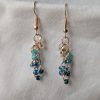 Ocean Tide earrings with 14 beads in seven ocean-inspired colors: clear, matte gray, pearly blue/gray, iridescent blue, metallic blue, matte deep blue, and solid indigo, connected with gold-colored jump rings and hooks.
