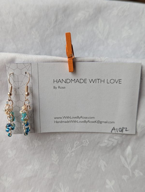 Ocean Tide earrings with 14 beads in seven ocean-inspired colors: clear, matte gray, pearly blue/gray, iridescent blue, metallic blue, matte deep blue, and solid indigo, connected with gold-colored jump rings and hooks.