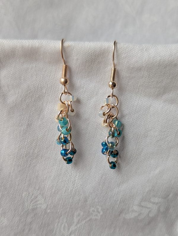 Ocean Tide earrings with 14 beads in seven ocean-inspired colors: clear, matte gray, pearly blue/gray, iridescent blue, metallic blue, matte deep blue, and solid indigo, connected with gold-colored jump rings and hooks.