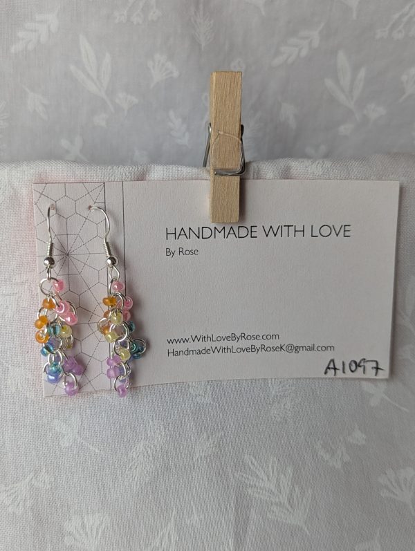 Handmade dangle earrings with 18 transparent pearly pastel beads in pink, orange, yellow, blue, periwinkle, and purple on silver-colored jump rings and earring hooks.