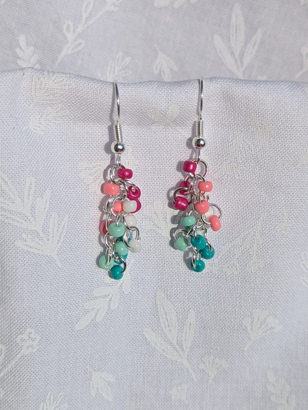 Tropical Breeze Earrings: Handmade earrings featuring 15 glass seed beads in teal, seafoam green, white, salmon pink, and fuchsia, arranged on silver-colored jump rings with matching earring hooks.