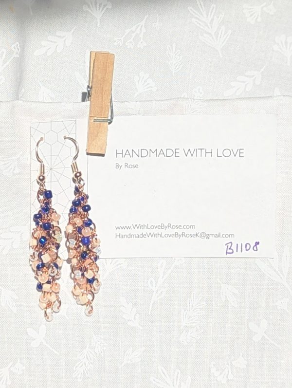 Moonlit Indigo: A pair of handmade earrings with 45 glass beads in shades of navy, dark blue, cream, and white, connected with rose-gold jump rings and hooks.
