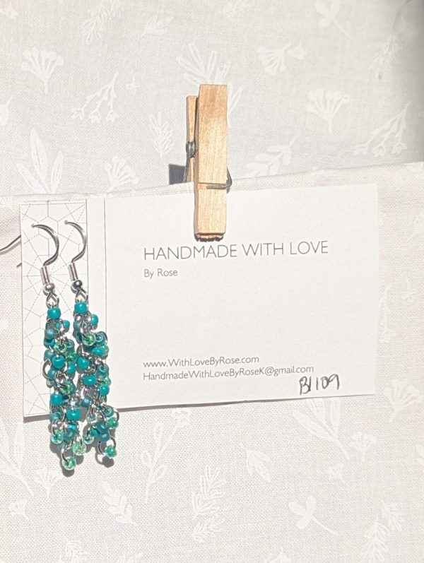 Forest Whispers — Handmade earrings with 27 green beads in shimmering, solid, and green-lined clear tones, connected with steel-colored jump rings and matching hooks.