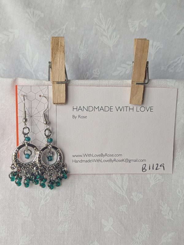 The Enchanted Forest Chandelier Earrings feature a Tibetan ornament, 12 beads in frosted, silver-lined, and matte iridescent deep emerald green.