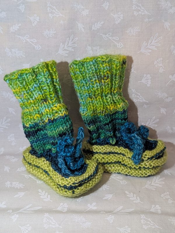 Bright green handknit baby booties with ribbed cuffs and teal blue ties, made from superwash merino wool.