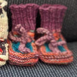 Multicolored baby booties in pink, purple, and turquoise with ribbed cuffs and soft pink ties, handknit for newborns.