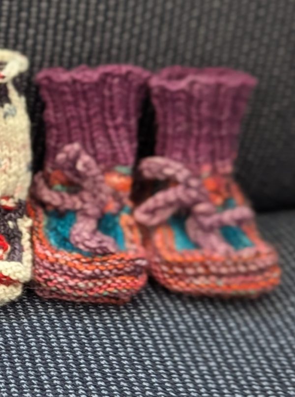 Multicolored baby booties in pink, purple, and turquoise with ribbed cuffs and soft pink ties, handknit for newborns.