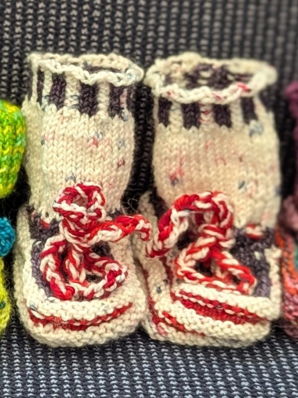 Peppermint Cream Holiday Baby Booties: Cream and brown handknit baby booties with red-and-white twisted ties, perfect for holiday newborns.