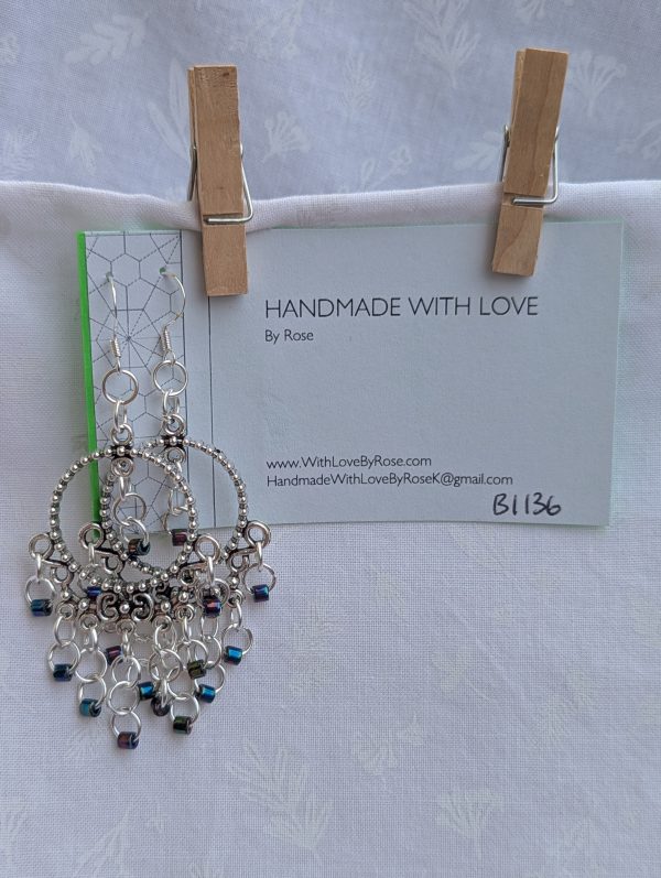 Moonlight Mirage Earrings: Pair of silver-colored hoop earrings with dangling silver jump rings and blue iridescent cylindrical beads.