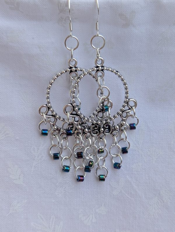 Moonlight Mirage Earrings: Pair of silver-colored hoop earrings with dangling silver jump rings and blue iridescent cylindrical beads.