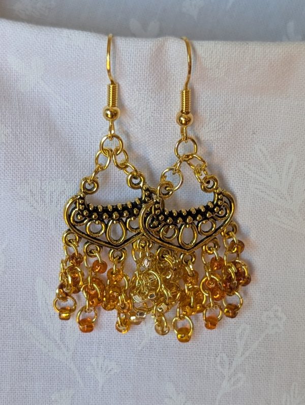 The Golden Hour Cascade Earrings: Pair of chandelier-style earrings with 25 glass beads in five shades and textures of gold, hung from antiqued gold ornaments with gold jump rings.