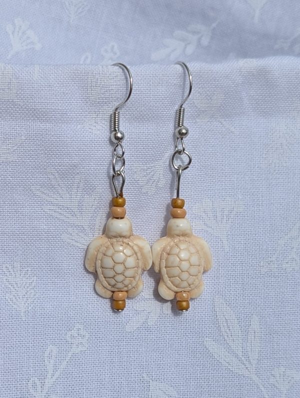 Desert Drift Turtle Earrings: Pair of earrings featuring beige turtle charms with tan and light brown beads on each side, connected by steel-colored findings.