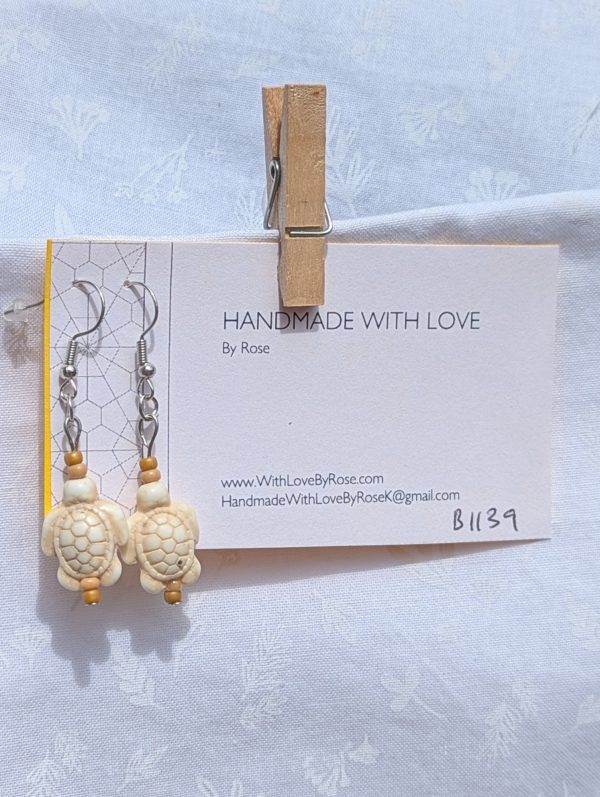 Desert Drift Turtle Earrings: Pair of earrings featuring beige turtle charms with tan and light brown beads on each side, connected by steel-colored findings.