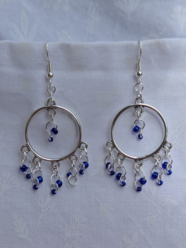 The Celestial Mobile Earrings: a pair of silver-colored hoop earrings with dangling silver jump rings and blue shiny glass beads