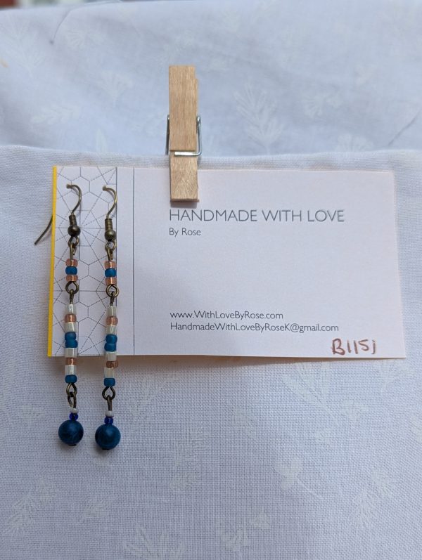 Moonlit Tides Earrings: Drop earrings featuring a capri blue focal bead accented by 14 small pearlescent white, silvery pink, and iridescent blue beads on bronze-colored findings.