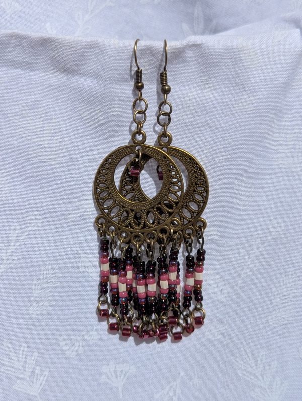 Desert Rose Sundial — Bronze filigree earrings with cascading glass beads in garnet, blush pink, ivory, rose, and crimson, arranged in five vertical strands.