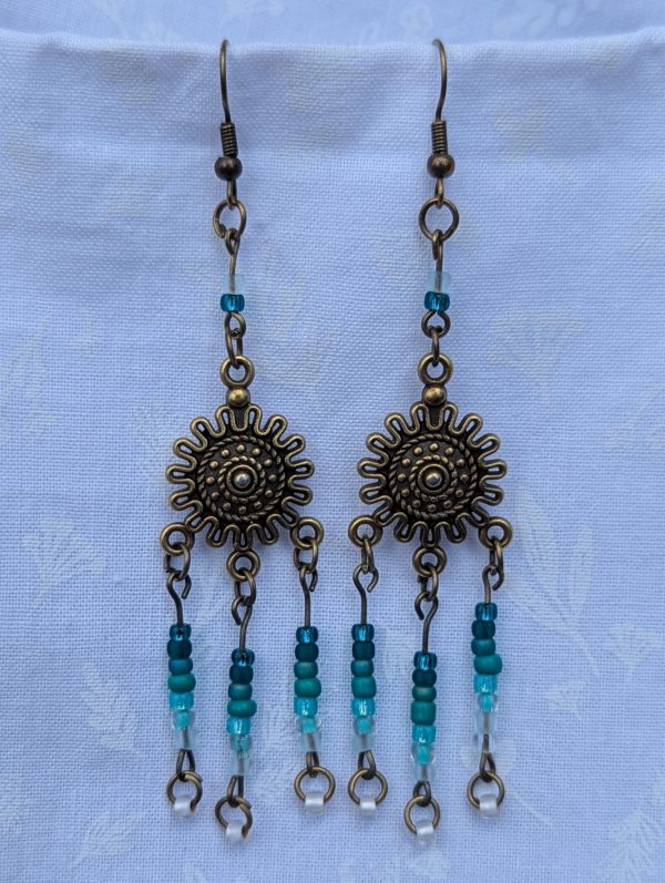 Sunburst Surf Earrings: Bronze sunburst earrings with hanging teal gradient beads in multiple shades.