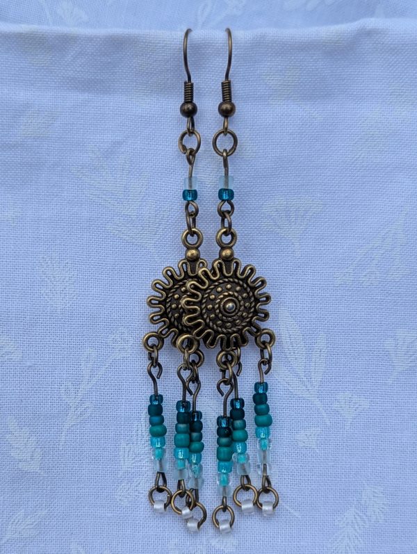 Sunburst Surf Earrings: Bronze sunburst earrings with hanging teal gradient beads in multiple shades.