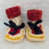 Handknit newborn baby booties in cream, red, and yellow with navy ties and a fiery red cuff, made from soft merino wool.