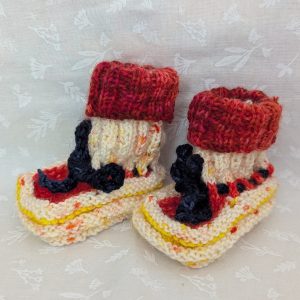 Handknit newborn baby booties in cream, red, and yellow with navy ties and a fiery red cuff, made from soft merino wool.