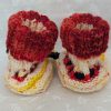 Handknit newborn baby booties in cream, red, and yellow with navy ties and a fiery red cuff, made from soft merino wool.