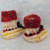 Handknit newborn baby booties in cream, red, and yellow with navy ties and a fiery red cuff, made from soft merino wool.