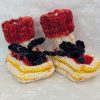 Handknit newborn baby booties in cream, red, and yellow with navy ties and a fiery red cuff, made from soft merino wool.
