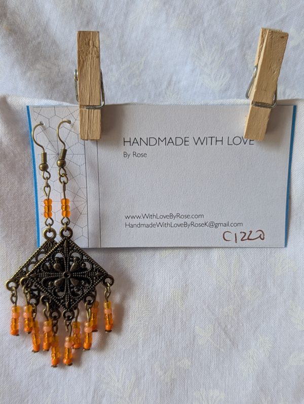 Orange beaded earrings, handcrafted with antiqued bronze square medallions and dangling orange glass beads in five textures, including translucent, frosted, and satin finishes. Hung on bronze ear hooks.