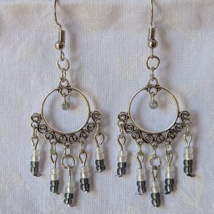 Pair of black and white earrings, handcrafted with silver crescent filigree hoops and dangling glass beads in a white-to-black gradient, including opal, frosted, matte, smoky, and black finishes. Hung on silver hooks.