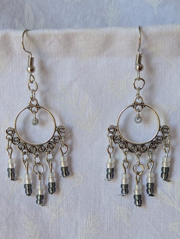 Pair of black and white earrings, handcrafted with silver crescent filigree hoops and dangling glass beads in a white-to-black gradient, including opal, frosted, matte, smoky, and black finishes. Hung on silver hooks.