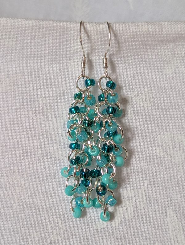 Pair of handmade teal dangle earrings with 27 seafoam, silver-lined teal, and iridescent cyan beads linked by silver rings and sterling silver hooks.