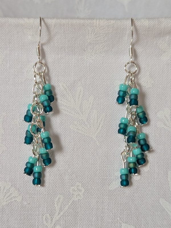 Ocean Whisper Earrings: A pair of handmade teal dangle earrings with 27 seafoam, silver-lined, and iridescent cyan beads. Suspended on silver jump rings with sterling silver hooks.