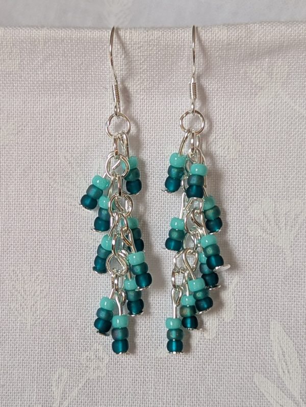 Ocean Whisper Earrings: A pair of handmade teal dangle earrings with 27 seafoam, silver-lined, and iridescent cyan beads. Suspended on silver jump rings with sterling silver hooks.