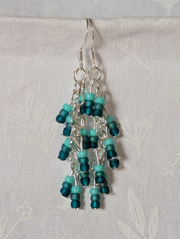 Ocean Whisper Earrings: A pair of handmade teal dangle earrings with 27 seafoam, silver-lined, and iridescent cyan beads. Suspended on silver jump rings with sterling silver hooks.