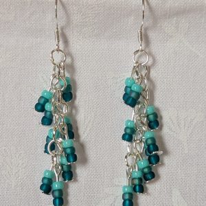 Ocean Whisper Earrings: A pair of handmade teal dangle earrings with 27 seafoam, silver-lined, and iridescent cyan beads. Suspended on silver jump rings with sterling silver hooks.