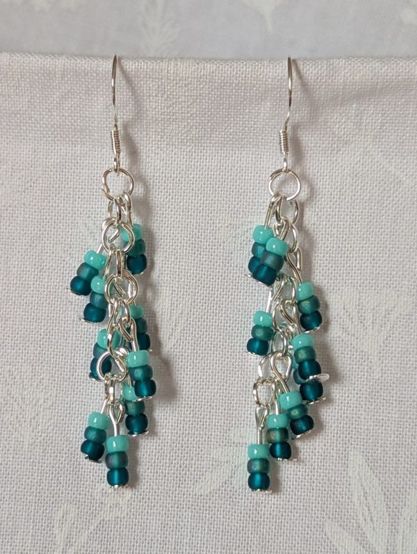 Ocean Whisper Earrings: A pair of handmade teal dangle earrings with 27 seafoam, silver-lined, and iridescent cyan beads. Suspended on silver jump rings with sterling silver hooks.
