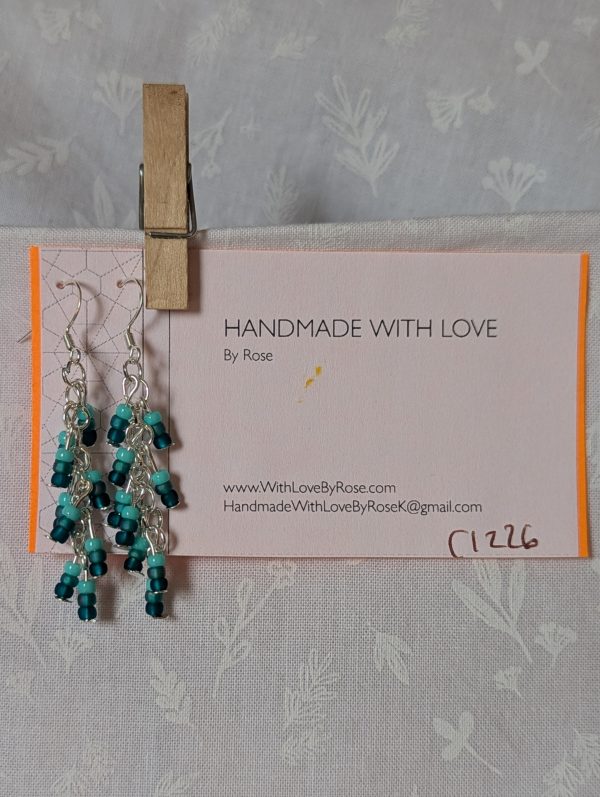 Ocean Whisper Earrings: A pair of handmade teal dangle earrings with 27 seafoam, silver-lined, and iridescent cyan beads. Suspended on silver jump rings with sterling silver hooks.