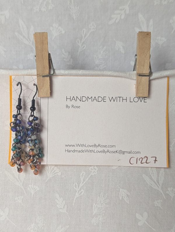 Handmade galaxy-themed earrings with 24 iridescent beads in 8 celestial colors, suspended on tungsten-colored rings with black hooks.