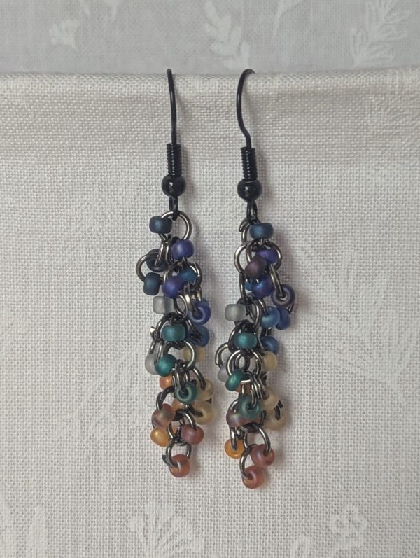 Handmade galaxy-themed earrings with 24 iridescent beads in 8 celestial colors, suspended on tungsten-colored rings with black hooks.