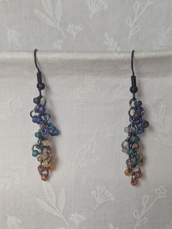 Handmade galaxy-themed earrings with 24 iridescent beads in 8 celestial colors, suspended on tungsten-colored rings with black hooks.