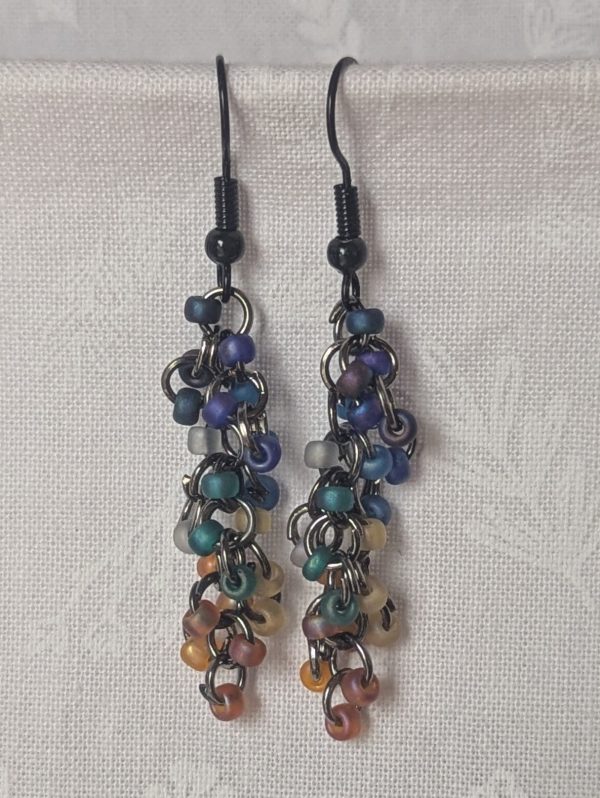 Handmade galaxy-themed earrings with 24 iridescent beads in 8 celestial colors, suspended on tungsten-colored rings with black hooks.