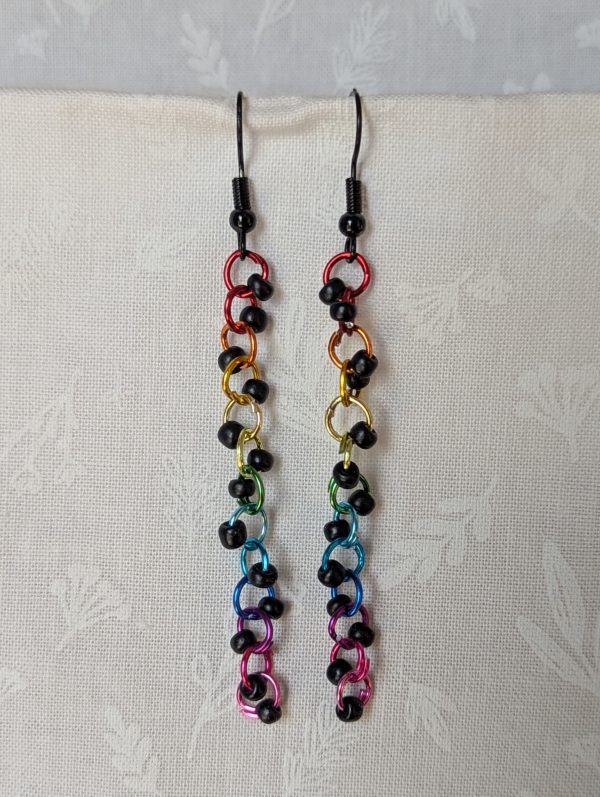 Dark Prism Earrings featuring 13 matte black beads and rainbow-colored jump rings from red to pink, hanging from black earring hooks.