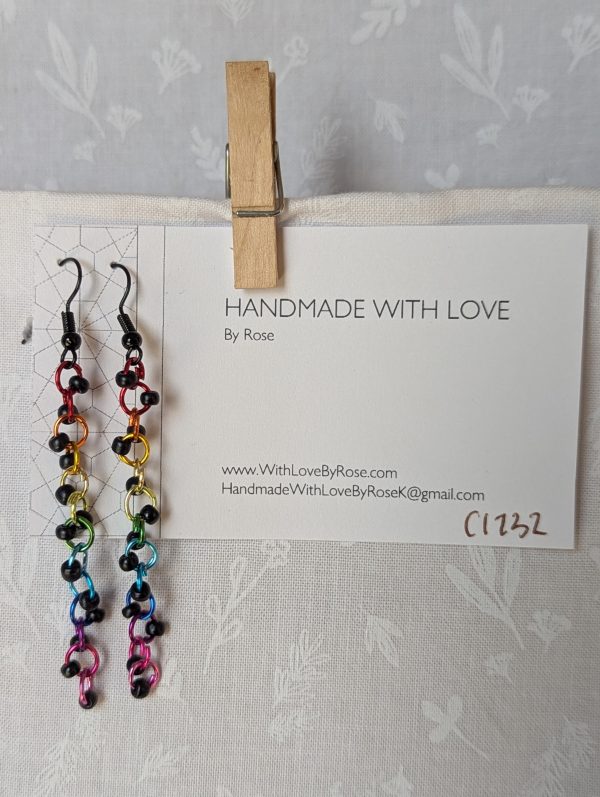 Dark Prism Earrings featuring 13 matte black beads and rainbow-colored jump rings from red to pink, hanging from black earring hooks.