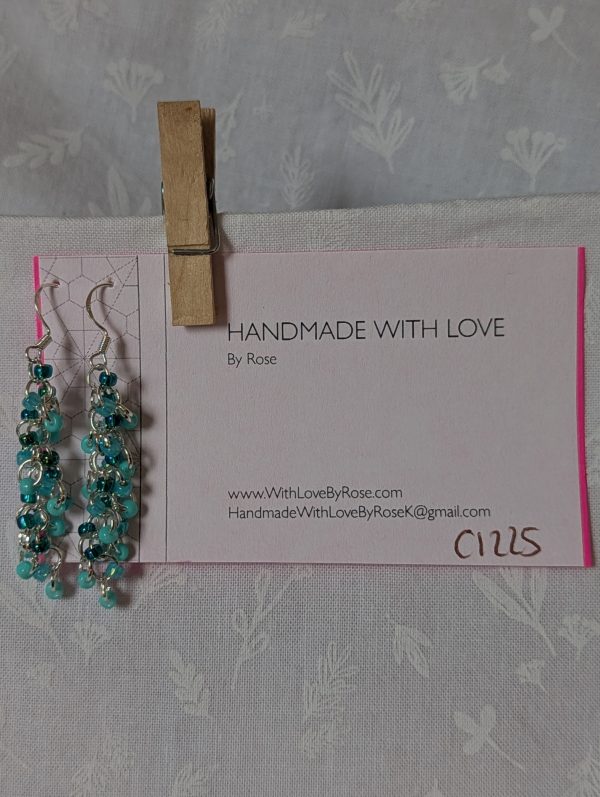 Pair of handmade teal dangle earrings with 27 seafoam, silver-lined teal, and iridescent cyan beads linked by silver rings and sterling silver hooks.