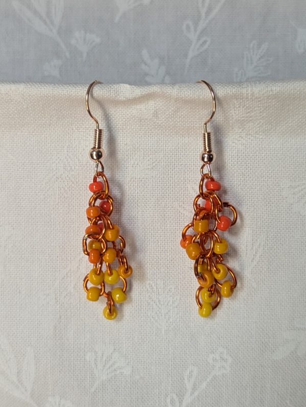Handmade dangle earrings with 18 orange and yellow glass beads in six warm shades, linked with orange jump rings and rose gold-colored hooks.